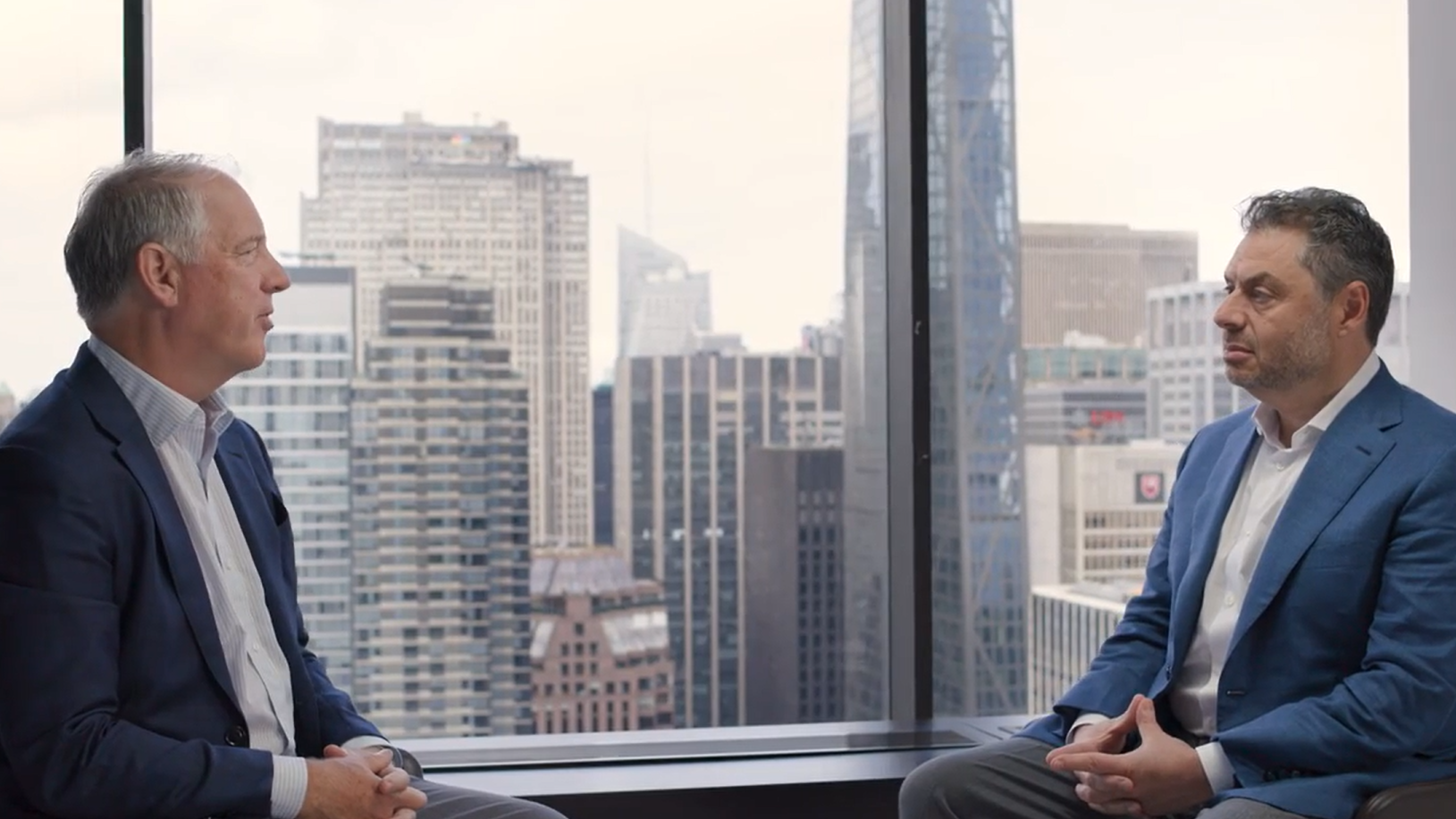 In Conversation with Jim Zelter & Eric Needleman Jim Zelter and Eric Needleman sit across from each other in a modern office overlooking a city skyline, engaged in a discussion on private credit, capital solutions, and evolving strategies within asset management and private markets.