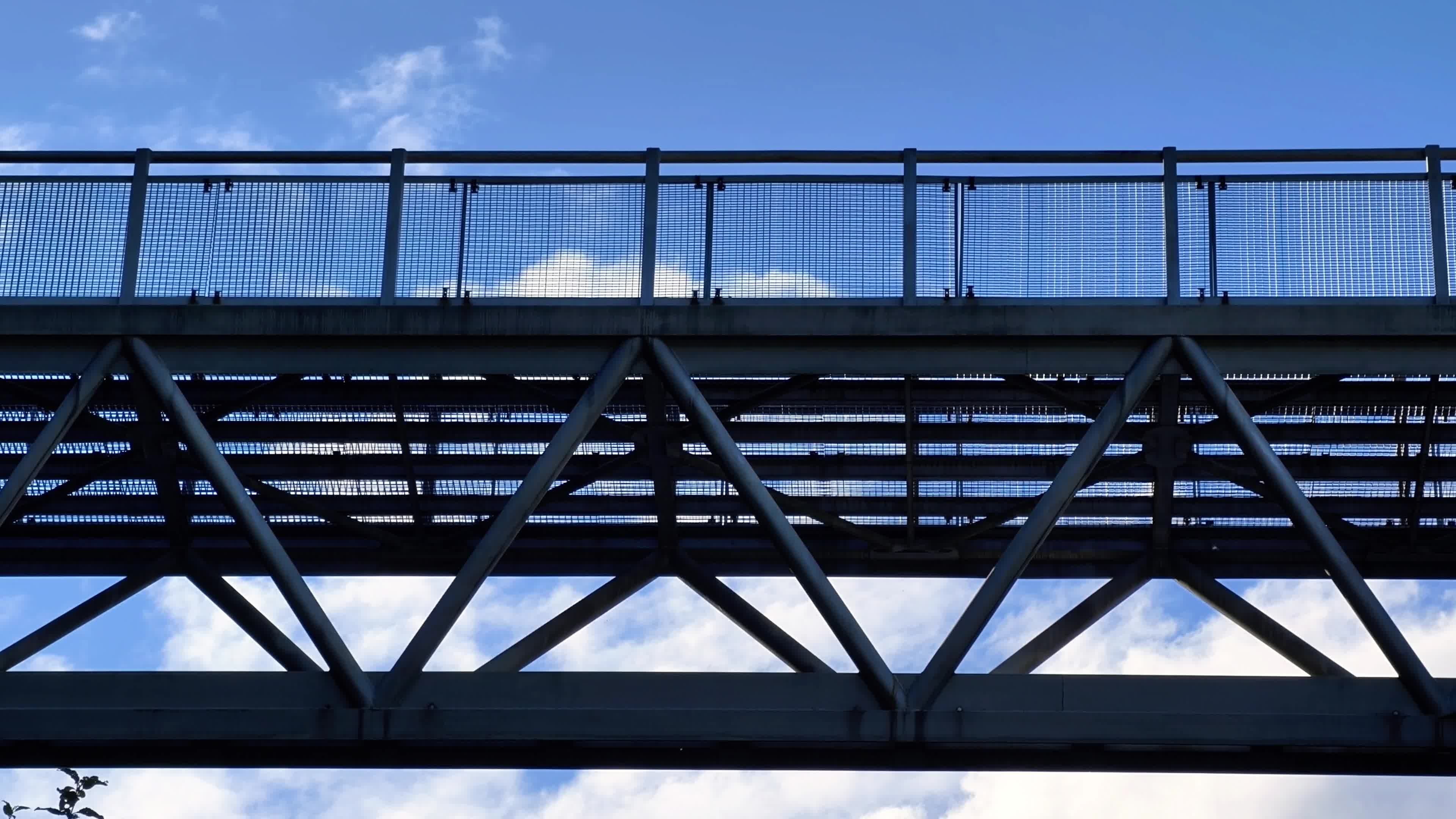 Private Market Secondaries: A Core Allocation for Modern Private Market Portfolios Steel bridge or elevated walkway structure viewed from below against a blue sky with clouds, featuring intersecting beams and railings, symbolizing infrastructure and connectivity within private markets and investment frameworks.