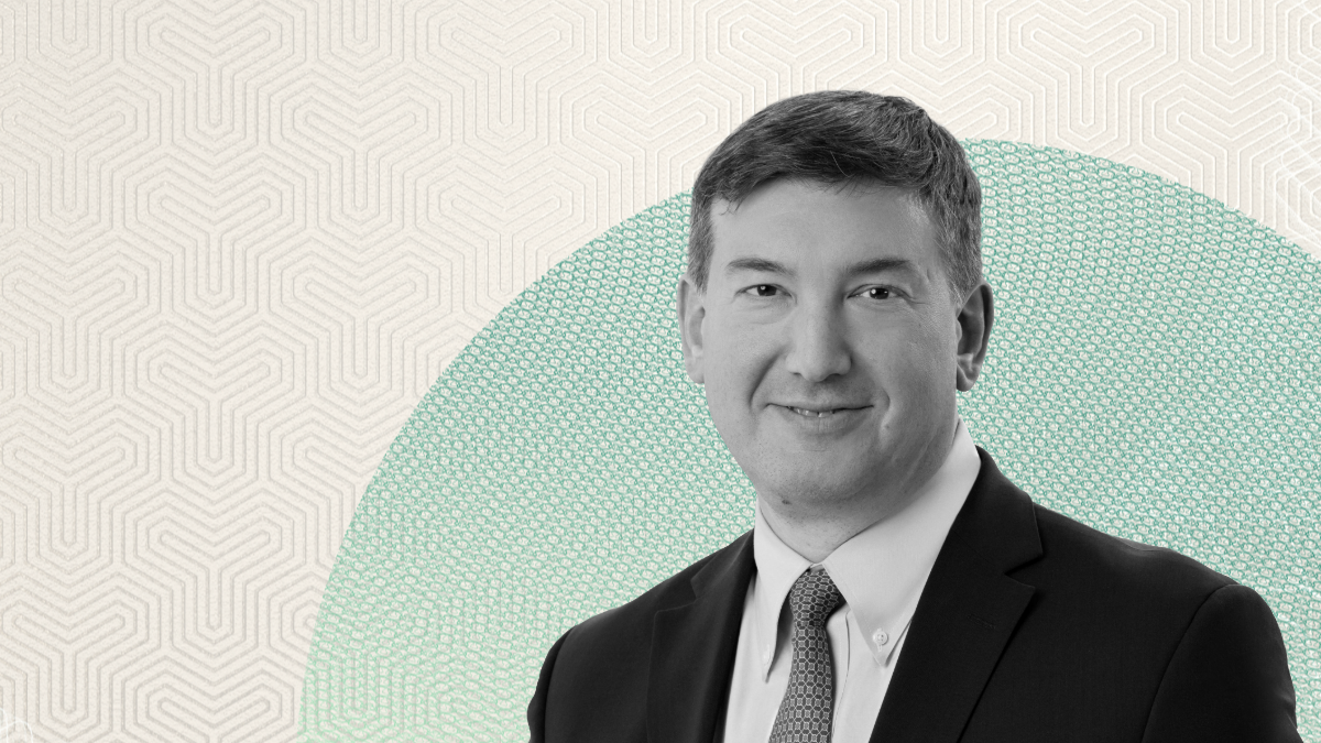 Apollo’s 13th Employee on the Firm’s Evolution and Principal Investor Mindset Black-and-white portrait of Scott Kleinman in a suit and tie, shown against a patterned beige and teal graphic background, used in Apollo’s leadership reflection content.